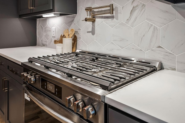 kitchen with decorative backsplash, light countertops, dark cabinetry, and stainless steel gas range oven