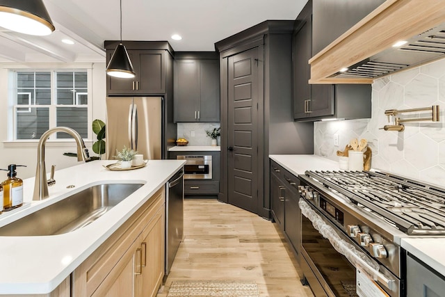 kitchen featuring premium range hood, light wood finished floors, a sink, appliances with stainless steel finishes, and decorative light fixtures