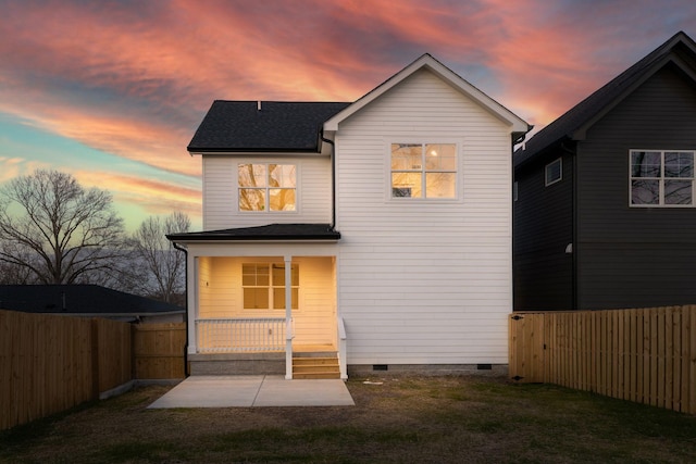 back of property at dusk featuring a yard, a fenced backyard, covered porch, a shingled roof, and crawl space