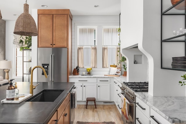 kitchen featuring high end appliances, brown cabinetry, a sink, white cabinetry, and light wood-type flooring