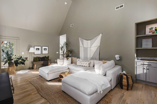 living area with visible vents, high vaulted ceiling, and light wood-style floors