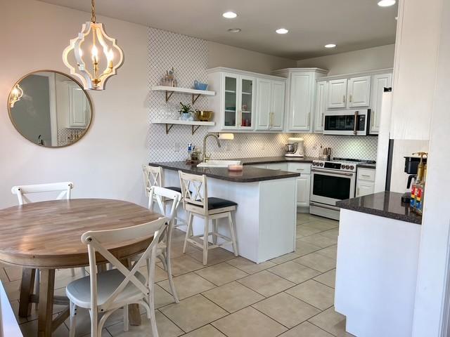 kitchen with a peninsula, a sink, white cabinets, appliances with stainless steel finishes, and dark countertops