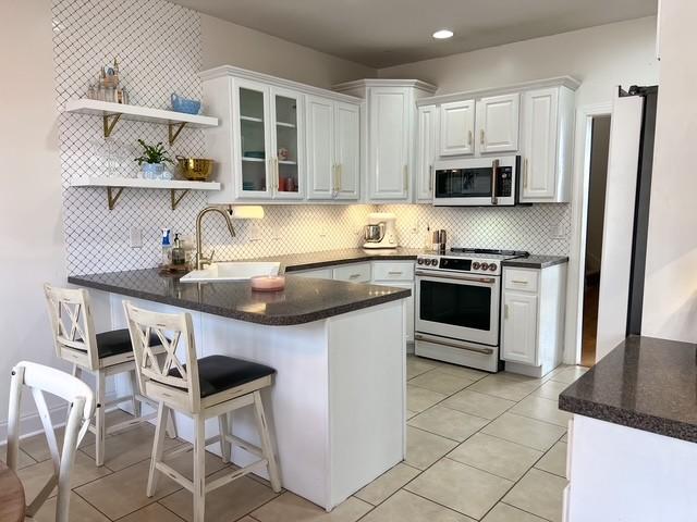 kitchen with high quality range, a peninsula, open shelves, a sink, and white cabinetry