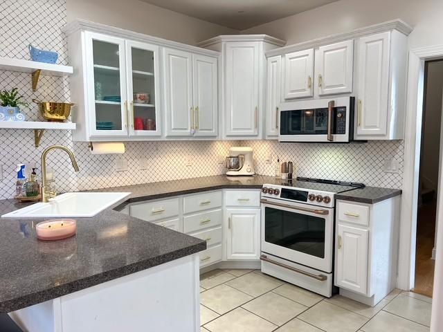 kitchen featuring open shelves, high end white range, a peninsula, white cabinetry, and a sink