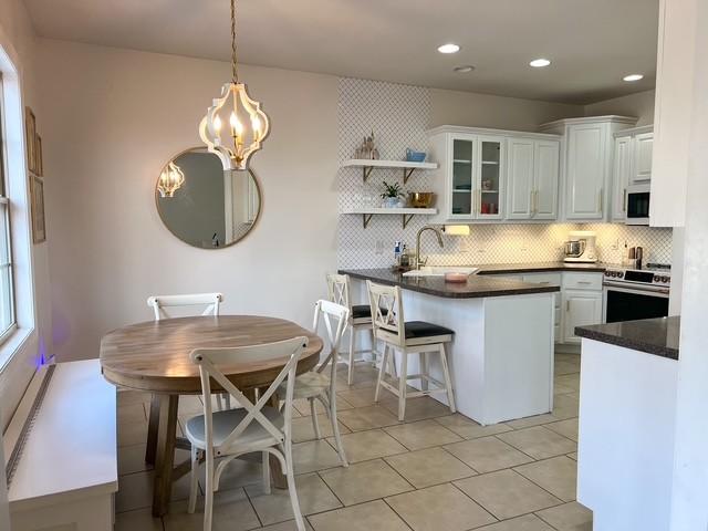 kitchen featuring white microwave, a peninsula, a sink, stainless steel range with electric stovetop, and dark countertops