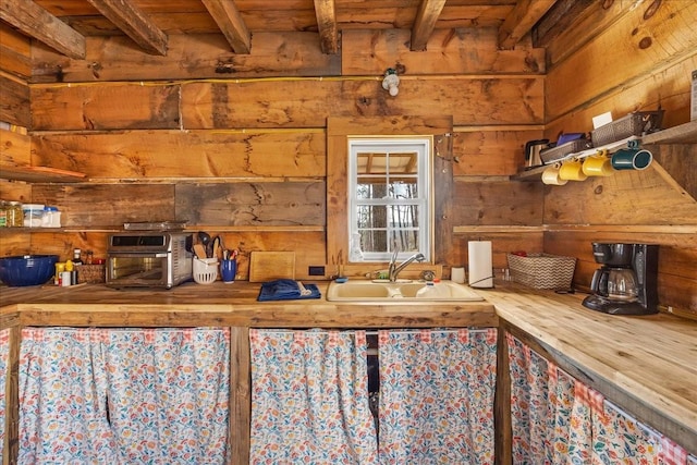 kitchen featuring beam ceiling, wooden ceiling, wood walls, and a sink