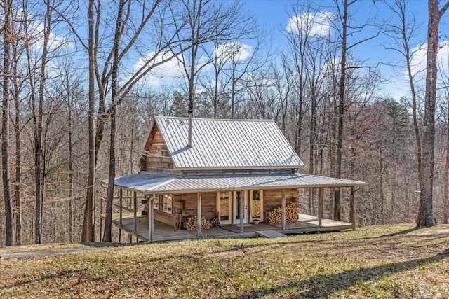 view of front of house featuring a front lawn, a wooded view, metal roof, a carport, and log exterior