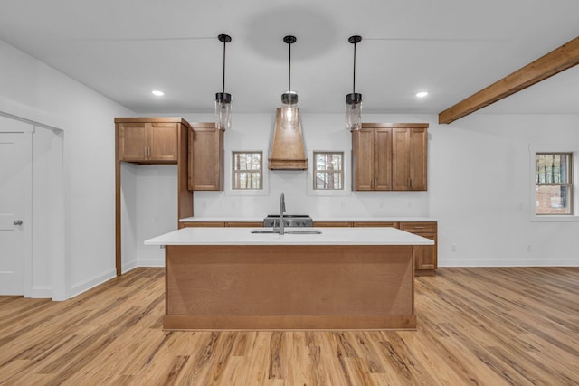 kitchen with a sink, brown cabinets, a center island with sink, and light countertops