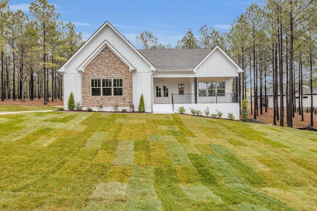 modern farmhouse style home with a front lawn, stone siding, board and batten siding, covered porch, and a shingled roof