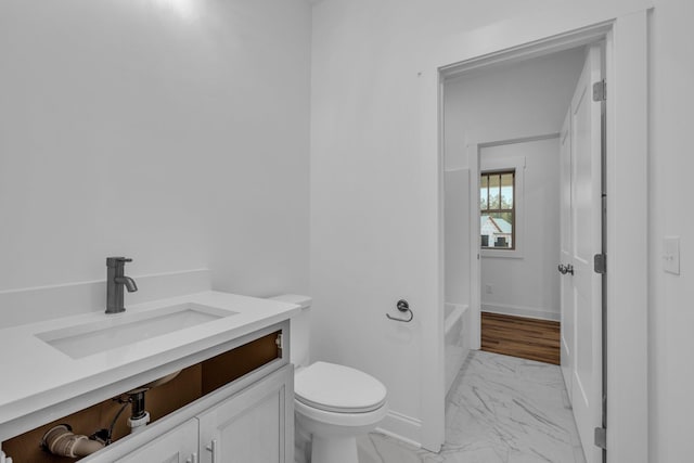 full bathroom with baseboards, toilet, a tub to relax in, marble finish floor, and vanity