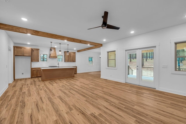 kitchen with ceiling fan, open floor plan, custom range hood, brown cabinets, and light wood-style flooring