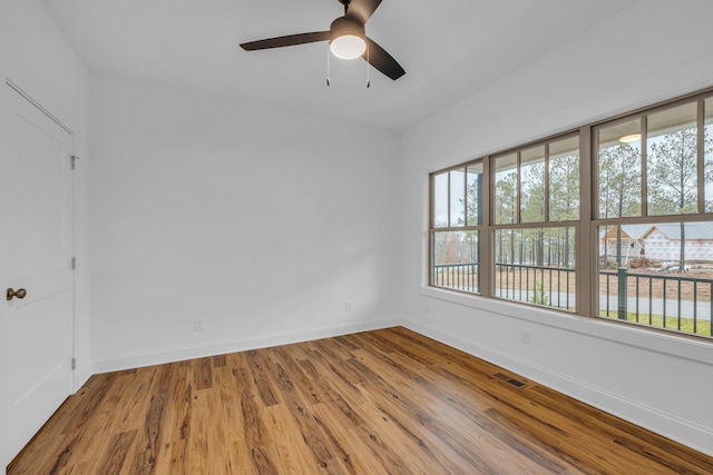 empty room with a ceiling fan, wood finished floors, visible vents, and a healthy amount of sunlight