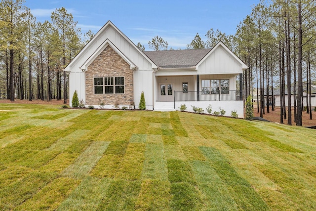 modern farmhouse style home featuring a front yard, a porch, board and batten siding, and stone siding