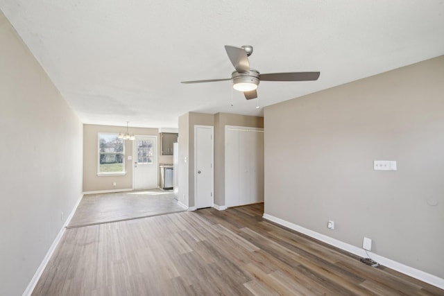 unfurnished living room featuring baseboards, wood finished floors, and ceiling fan with notable chandelier