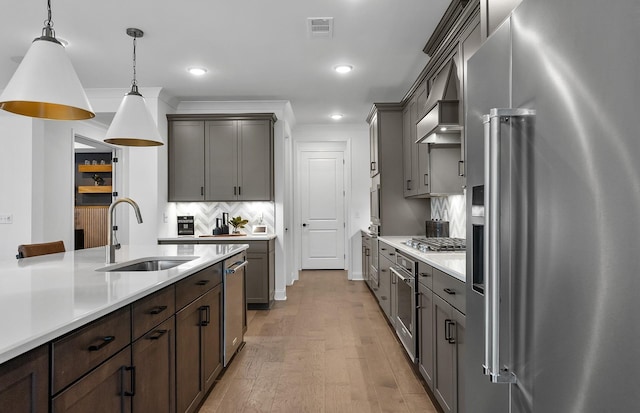 kitchen featuring light wood finished floors, a sink, stainless steel appliances, light countertops, and decorative light fixtures