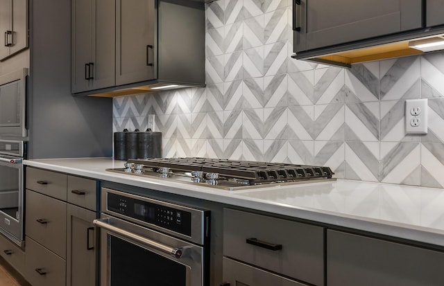 kitchen featuring light countertops, backsplash, appliances with stainless steel finishes, and gray cabinetry