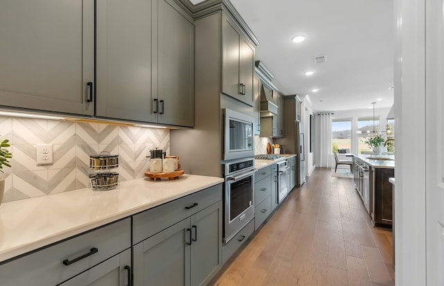 kitchen with light wood-type flooring, a sink, backsplash, stainless steel appliances, and light countertops