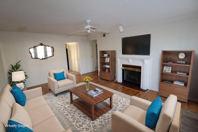 living room featuring ornamental molding, a fireplace with flush hearth, wood finished floors, and ceiling fan