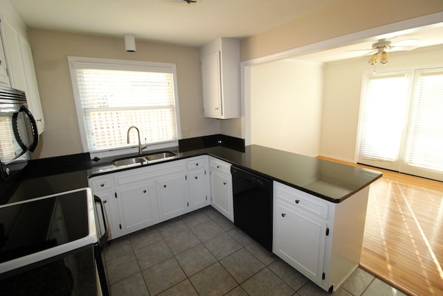 kitchen with dark countertops, a peninsula, plenty of natural light, black appliances, and a sink