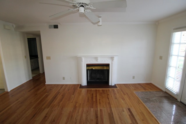 unfurnished living room with visible vents, a fireplace with flush hearth, ornamental molding, wood finished floors, and a ceiling fan