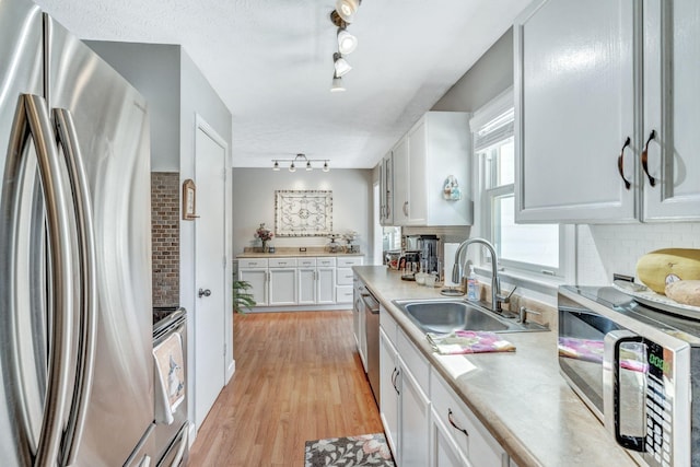 kitchen with light wood-type flooring, light countertops, white cabinets, stainless steel appliances, and a sink