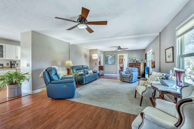 living area featuring baseboards, a textured ceiling, wood finished floors, and a ceiling fan