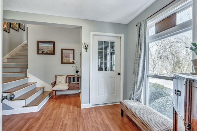 entrance foyer with stairs, baseboards, light wood-type flooring, and a textured ceiling