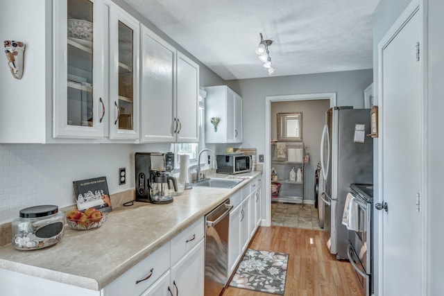 kitchen featuring light countertops, stainless steel appliances, light wood-style floors, white cabinetry, and a sink