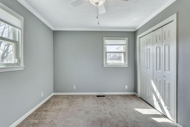 unfurnished bedroom with carpet, visible vents, baseboards, ornamental molding, and a closet