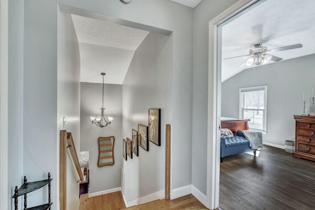 corridor featuring stairway, wood finished floors, baseboards, an inviting chandelier, and vaulted ceiling