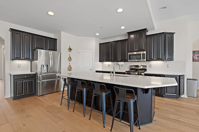 kitchen featuring a sink, light wood-type flooring, appliances with stainless steel finishes, arched walkways, and a kitchen island with sink