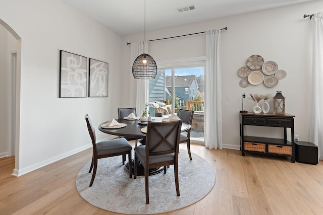 dining area with light wood-type flooring, visible vents, arched walkways, and baseboards