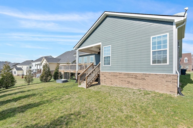 rear view of property with a deck, a yard, brick siding, and stairs