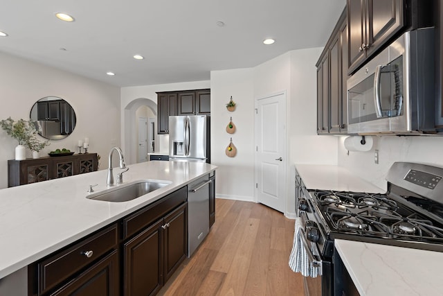 kitchen with light wood finished floors, recessed lighting, arched walkways, stainless steel appliances, and a sink