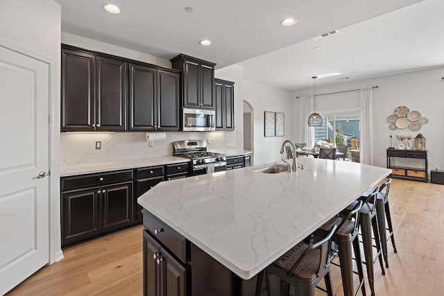 kitchen featuring a center island with sink, visible vents, arched walkways, a sink, and stainless steel appliances