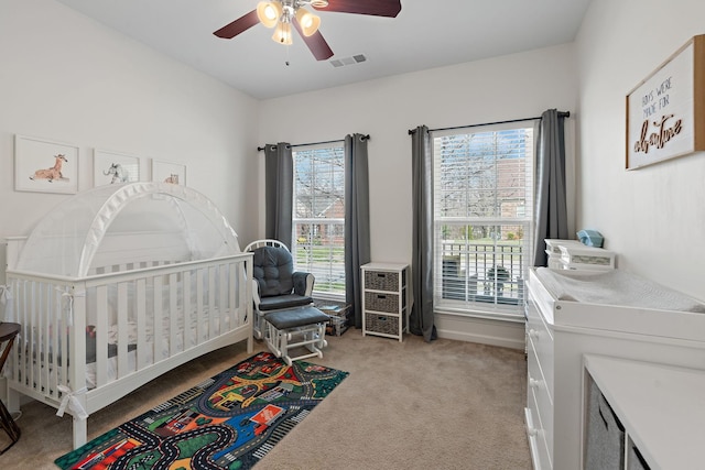 bedroom featuring visible vents, light carpet, a nursery area, and ceiling fan