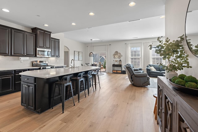 kitchen featuring light wood-style flooring, a sink, arched walkways, appliances with stainless steel finishes, and a breakfast bar area