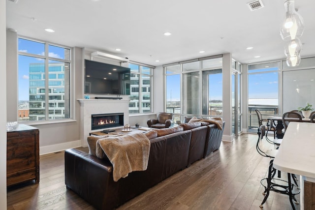 living room with hardwood / wood-style floors, a glass covered fireplace, visible vents, and a wealth of natural light