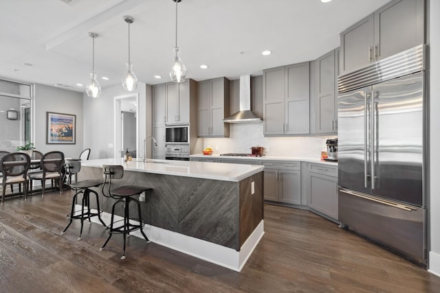 kitchen featuring built in appliances, gray cabinets, wall chimney range hood, and dark wood-style flooring