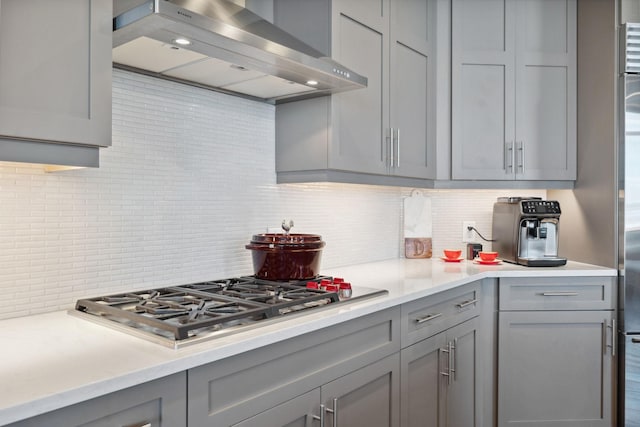 kitchen featuring backsplash, gray cabinetry, light countertops, stainless steel gas stovetop, and wall chimney exhaust hood