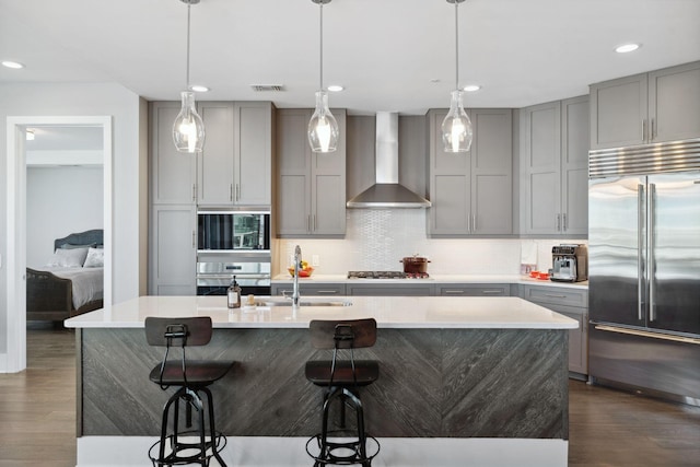 kitchen featuring dark wood-type flooring, appliances with stainless steel finishes, gray cabinetry, and wall chimney range hood