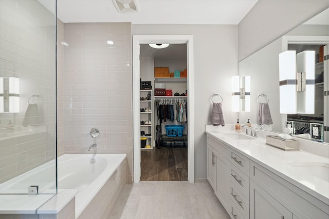 full bathroom featuring a spacious closet, tiled tub, double vanity, tiled shower, and a sink