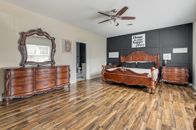 bedroom featuring wood finished floors, baseboards, visible vents, ceiling fan, and a decorative wall