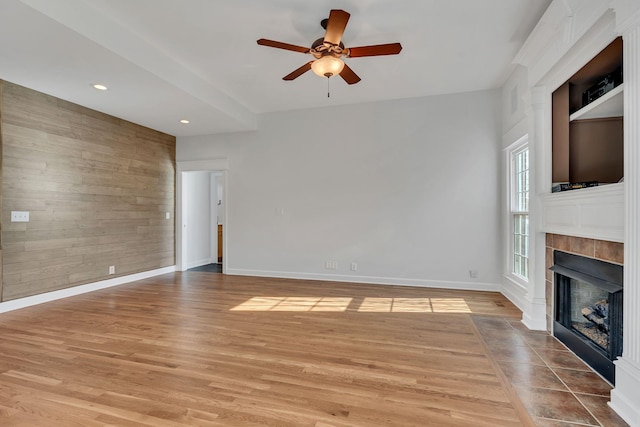 unfurnished living room featuring baseboards, a fireplace, ceiling fan, wood walls, and light wood-type flooring