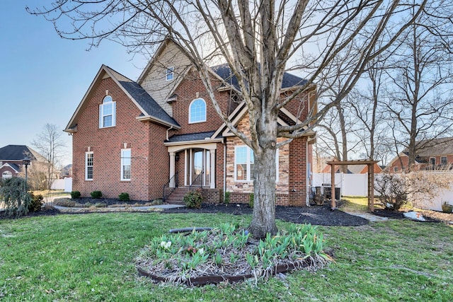 traditional home featuring brick siding, a shingled roof, a front lawn, and fence