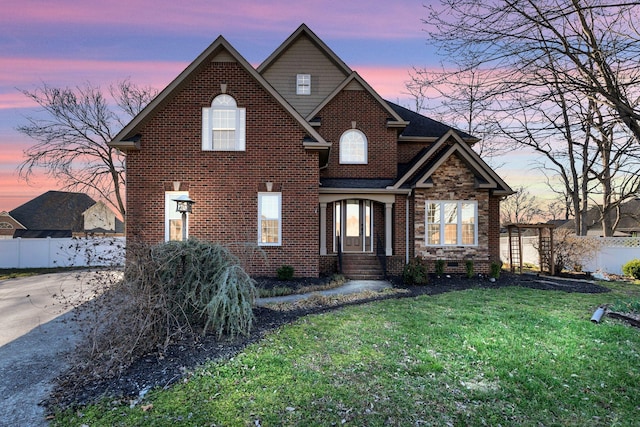 traditional-style home with driveway, a lawn, brick siding, and fence