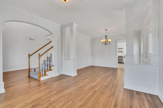 empty room with ornamental molding, stairway, light wood-style floors, an inviting chandelier, and a decorative wall