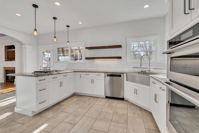 kitchen featuring decorative backsplash, stone counters, appliances with stainless steel finishes, white cabinets, and a sink