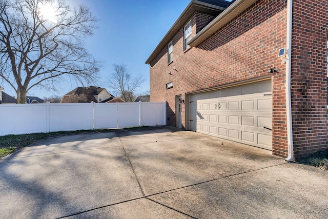 view of home's exterior with a garage, fence, brick siding, and driveway