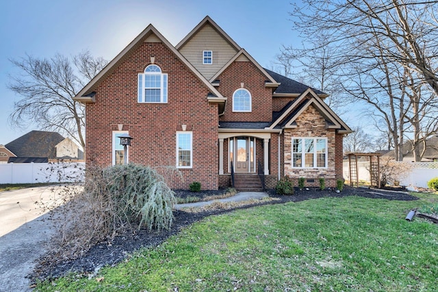 view of front of house with brick siding, a front lawn, fence, roof with shingles, and stone siding